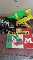 Photo showing Meccano box, Metal Earth model kit, and yellow-green LaRam toy gun.