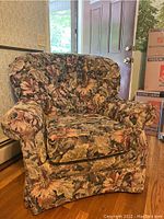 Front view of the floral upholstered arm chair indoors near a door with moving boxes in the background.