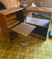 Photo showing two wooden shelving units and a pedestal nightstand on patterned carpet. The shelving units exhibit wood grain patterns; rolling shelf has caster wheels, bookcase shows wear on lower edge.