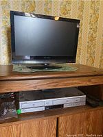 Dynex 19-inch LCD TV on wooden furniture with patterned wallpaper background.