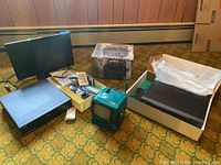 Overview of the lot showing the Apex DVD player, Curtis TV, boxed GPX CD player, Dynex TV, assorted remotes, and a box of tapes.