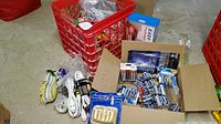 Lot of extension cords, batteries, ceramic holder and other household maintenance hardware in box and red plastic milk crate on basement floor