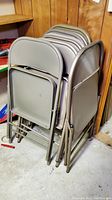 Nine beige/tan metal folding chairs stacked and folded, showing wear and storage in basement area.