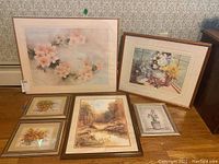 Six framed prints arranged on a table, showing the variety of floral and landscape images and frame styles.