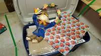 Storage bin open with floral wrapping paper, cardboard boxes, gift bags, and a small scarecrow figurine visible