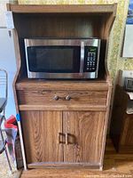 Front view of woodgrain composite laminate kitchen cabinet hutch with microwave placed on upper shelf, showing drawer with two knobs and double-door cabinet below.