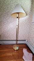 Full view of the 58-inch floor lamp with beige conical lampshade and brass body, standing on wood floor against floral wallpaper.