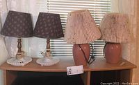 Four lamps displayed on wood surface, two with hobnail milk glass bases and two with pink ceramic bases.