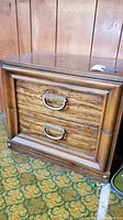 Front view of a wooden nightstand with two drawers and brass-tone curved handles, showing the overall condition and design details.