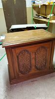 Front and side view of wood nightstand cabinet showing carved front doors and worn top surface with scratches.