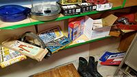 Shelf with various drill bit kits, hardware boxes, black rubber boots, and packaging materials scattered around.