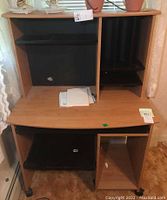 Front view of the Sauder rolling work desk showing woodgrain laminate surface, upper shelves and compartments, small paint spot on upper shelf, and lower open shelves.