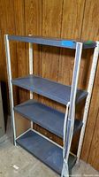 Front view of the 4-tier metal shelf unit showing the gray shelves and white vertical supports. Visible scratches on the metal.