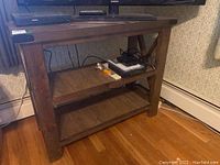 Full front view of three-tier wooden shelf unit with objects on the middle shelf under a TV.