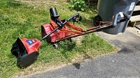 Toro Power Shovel laying on grass and pavement with red body, black handle, and attached red extension cord