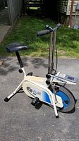 Full side view of the white and blue Voit ERGOMETER stationary exercise bike showing the seat, pedals, flywheel casing, and front control panel.