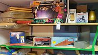 Shelf showing padded mailing envelopes stacked on the left, several boxed household items including a power washer attachment, hand vacuum, air mattress pump, and coffee thermos on the right.