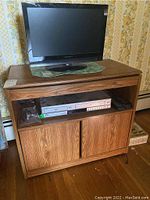 TV console cabinet with wood finish, flat rotating top, open middle shelf holding video equipment, and closed bottom cabinet with sliding doors.