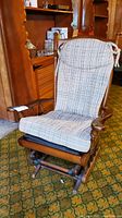 Front view of the vintage wooden glider rocking chair with plaid cushion showing seat, back, and armrest detail.