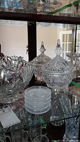 Large pinwheel pattern crystal candy bowl with lid and other glassware in the background on glass shelf