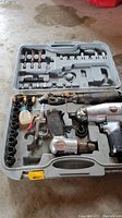 Full view of open mold case containing two silver air impact wrenches, air hammer, brass fittings, spray gun, various bits and accessories.