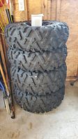 Stack of four ATV tires on wheels, showing full tread pattern and sidewalls