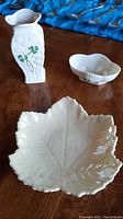 View of the three Belleek porcelain items on wooden surface: cream leaf dish, bud vase with shamrock, small dish.