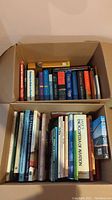 Top view of two cardboard boxes filled with various books including novels, reference and coffee table books