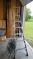 6 ft aluminum convertible ladder standing open in a garage with some black wire fencing in front.