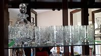 Glass shelf with decanter and eleven tumblers showing overall set.