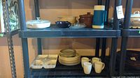 CorningWare and ceramic dishes with mugs and thermos on metal shelving