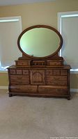 Front view of the oak dresser with attached oval mirror, showing all drawers and cabinet door.