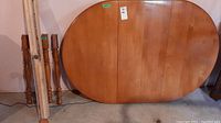 Photo of the oval wooden table top leaning against a wall with four wooden legs beside it