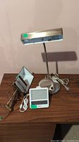Lot with a silver desk lamp, brass wall lamp, and Philips GoLite device on wooden surface