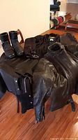 Photo showing the men's black leather jacket, leather vest, and leather chaps arranged on a table, along with the boots.