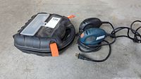 Photo of two Black & Decker electric mouse sanders side by side along with their black hard plastic carrying case on concrete flooring.