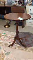 Full view of the antique wooden pedestal side table showing brass claw feet and curved legs on a carpeted surface.