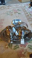 Photo of three stainless steel platters with matching small square bowl and Lagostina tea pot placed on the largest platter on a floral carpet.
