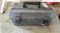 Closed black plastic toolbox on floor with handle and latches visible