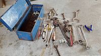 Metal blue toolbox with tools arranged on ground including wrenches, ratchets, drivers and pliers