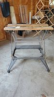 Front view of the adjustable work bench showing two wooden slats on a grey painted metal frame and base with footrest platform.