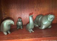 Four soapstone animal carvings on wooden shelf: parrot-like bird, owl-like bird, long-necked bird, walrus