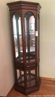 Full view of the wood and glass curio cabinet standing in a corner, showing the overall shape and design.