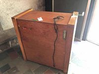 Side view of the wooden chicken incubator showing the front panel with latch and power cord hanging.