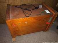 Wooden rectangular incubator box with power cord and light bulb on top, showing front and side exterior.