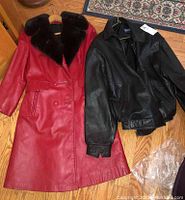 Top view of both jackets laid flat on floor, front side visible showing faux fur collar on red jacket and zippered black bomber jacket