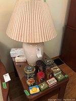 Table lamp on teak wood table with glass top, surrounded by assorted decorative tins.