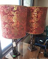 Pair of vintage table lamps with wood bases and red velveteen gold patterned shades on a table by a window