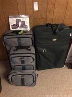 Overall photo showing all four luggage pieces: one large dark green suitcase and a set of three grey luggage bags with blue and black stripes.