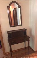 Front view of wooden hall table with drawer, vertical cubby storage compartments, metal rail on top, and casters beneath.